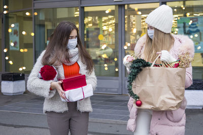 Young women in medical mask shopping for christmas in mall. xmas holidays in new covid-19 reality.