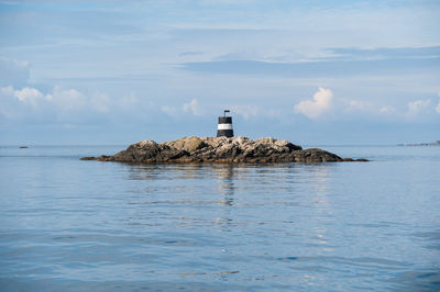 Lighthouse on sea by building against sky