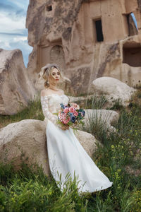 Full length of bride holding bouquet standing by stone