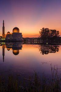 Scenic view of lake by buildings against sky during sunset