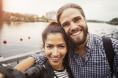 Portrait of smiling couple standing by river in city