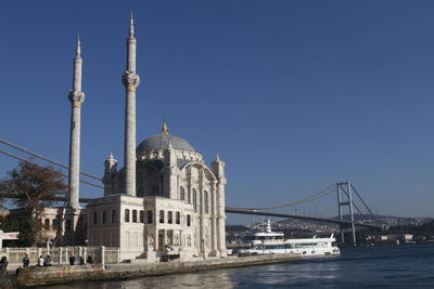 Ortakoy mosque by bosphorus bridge over strait against clear blue sky