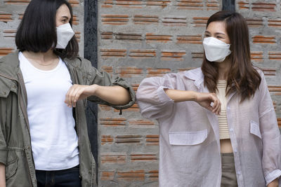 Full-body photo of two women wearing masks greet each other with an elbow bump