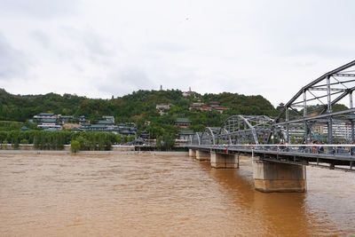 Bridge over river by buildings against sky