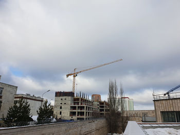 Crane by buildings against sky in city