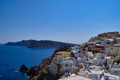 Scenic view of sea by buildings against clear blue sky