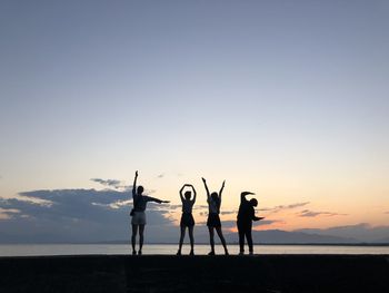 Silhouette friends making love text while standing at shore against sky during sunset