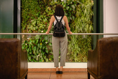 Full length rear view of young woman standing at window in hotel