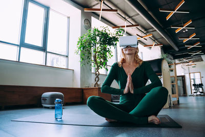 Smiling woman wearing virtual reality simulator doing yoga at home