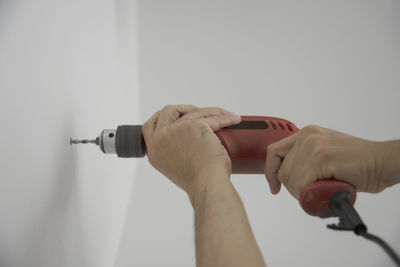 Close-up of hands holding drill on wall