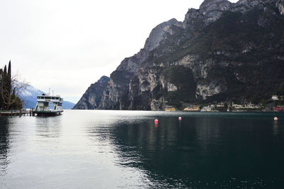 Boats moored on sea by mountain against sky