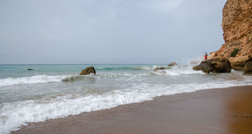 Scenic view of sea with man on rock against sky