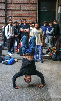 Full length of people looking at man performing handstand on floor