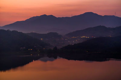 Scenic view of lake by silhouette mountains against orange sky