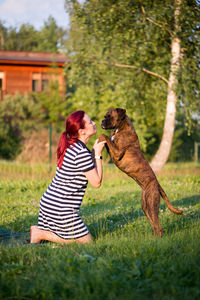 Mid adult woman playing with dog while kneeling on grassy field against sky at park