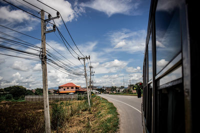 Road by electricity pylon against sky