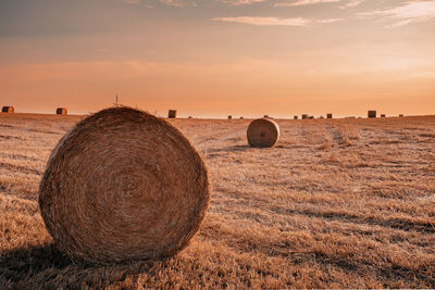 Hay bales on field against sky during sunset