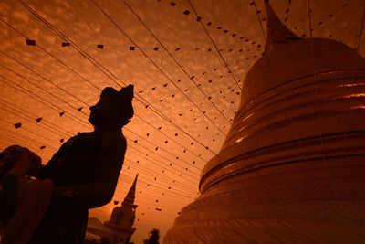 Low angle view of decorations and stature at temple against orange sky during sunset