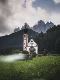 Church on grassy field with mountains in background against cloudy sky