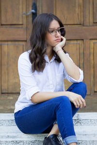 Young woman looking away while sitting on wall