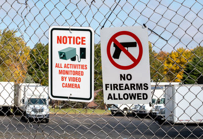 Signs on a chain link fence  says no firearms are allowed and video cameras are monitoring the area.