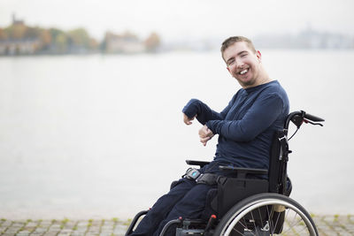 Portrait of happy man with cerebral palsy sitting on wheelchair by lake