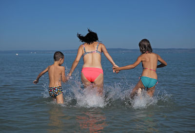 Rear view of friends standing on beach against clear sky