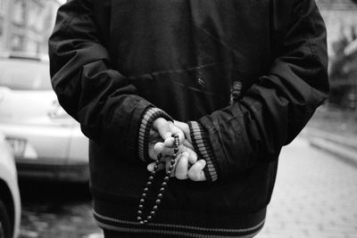 Midsection of man holding prayer beads while standing outdoors