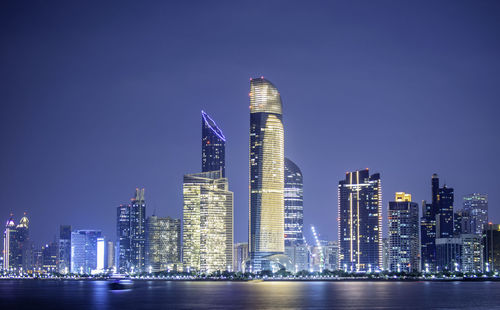 Illuminated modern buildings in city against sky at night