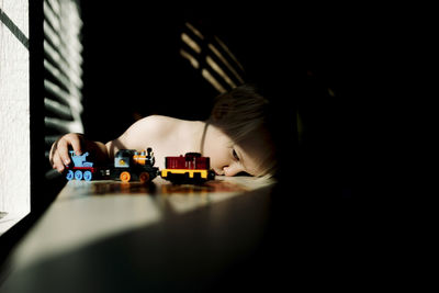 Boy playing with toy train while sitting at table by window
