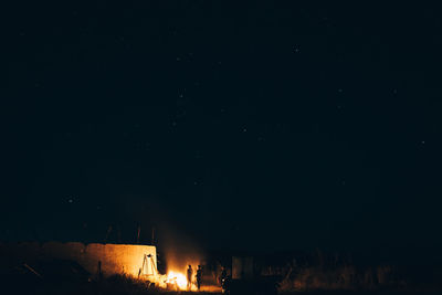 People standing by bonfire against sky at night