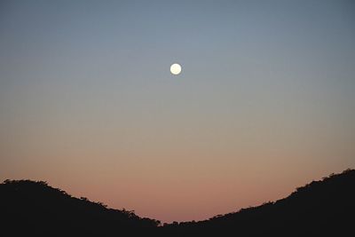 Low angle view of silhouette mountain against full moon in sky during sunset