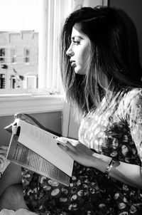 Beautiful woman sitting with novel while looking through window