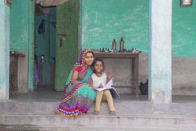 Portrait of smiling mother and daughter reading book in courtyard of the house in village india