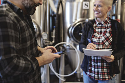 Smiling worker with spiral notebook discussing to male manager at brewery