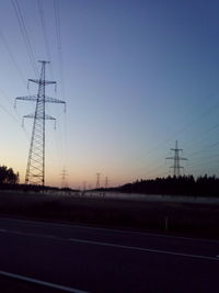 Electricity pylons on road against clear sky at sunset