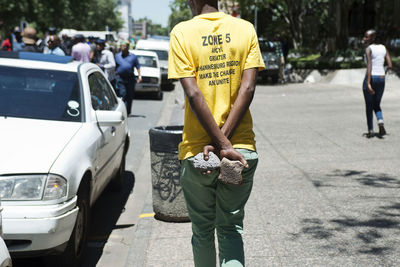 Rear view of man holding stones while walking on sidewalk