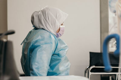 Side view of woman wearing mask and sitting on chair in hospital