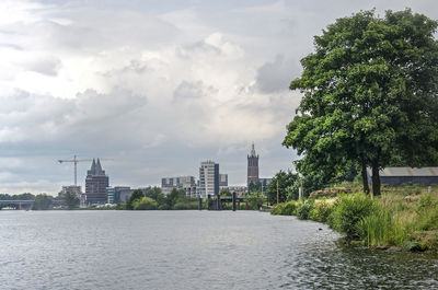 View of buildings by river against cloudy sky