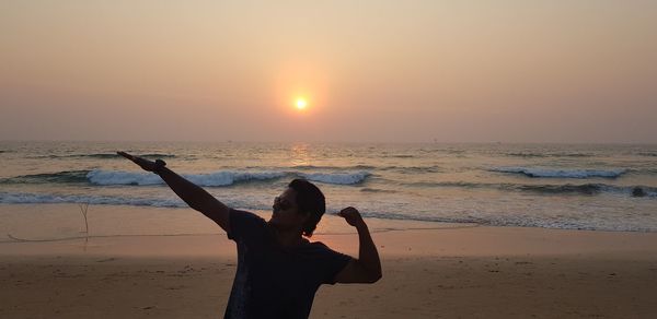 Man gesturing at beach against sky during sunset
