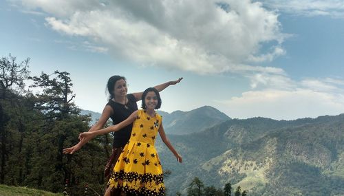 Portrait of daughter and mother with arms outstretched standing on mountain against sky