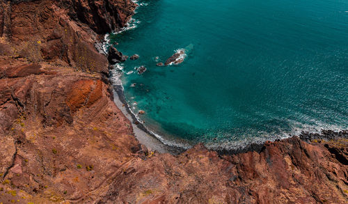 Atlantic ocean coastline, red cliffs, rocks, turquoise waves and sea foam. madeira island, portugal