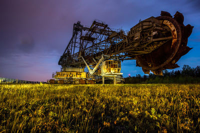 Old crane on field against cloudy sky