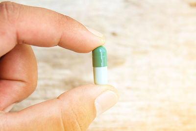 Cropped hand holding pill on table