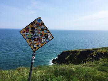 Stickers stuck on information sign at cliff walk against sea