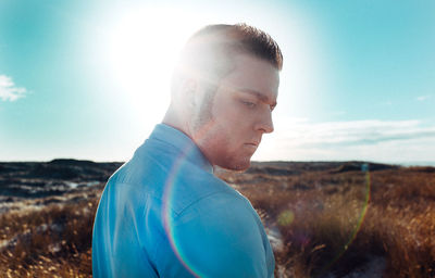 Close-up of thoughtful young man standing on field against sky