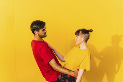 Side view of young couple standing against yellow wall