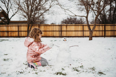 Blonde curly haired girl sitting outside in snow making snowman