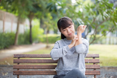 Young woman scratching hand while sitting on bench at park