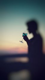 Silhouette man holding umbrella against sky during sunset